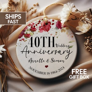 May include: Round white ceramic ornament with a floral design in shades of pink and red. The ornament features the text "40th Wedding Anniversary Annette & Simon November 18 1984-2024".