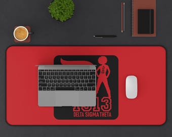 May include: A red desk mat with a black rectangular design featuring a silhouette of a woman, the Greek letters ΔΣΘ, and the number 13. The text "DELTA SIGMA THETA" is below. A laptop, mouse, and other office supplies are on the black surface.