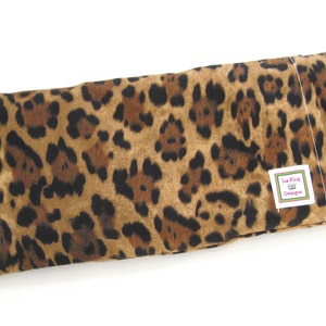 May include: A rectangular item with a leopard print pattern in shades of brown and black. It features a small white tag with the text "Lisa King Designs" and a crown logo. This could be a heat pack or pillow.