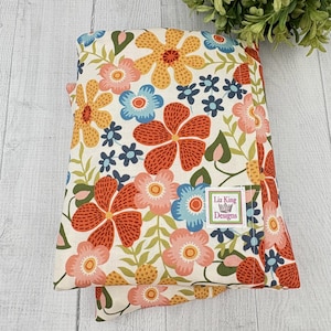 May include: Folded floral fabric with a cream background and a pattern of orange, pink, blue, and yellow flowers. The fabric has green leaves and the label "Liz King Designs".