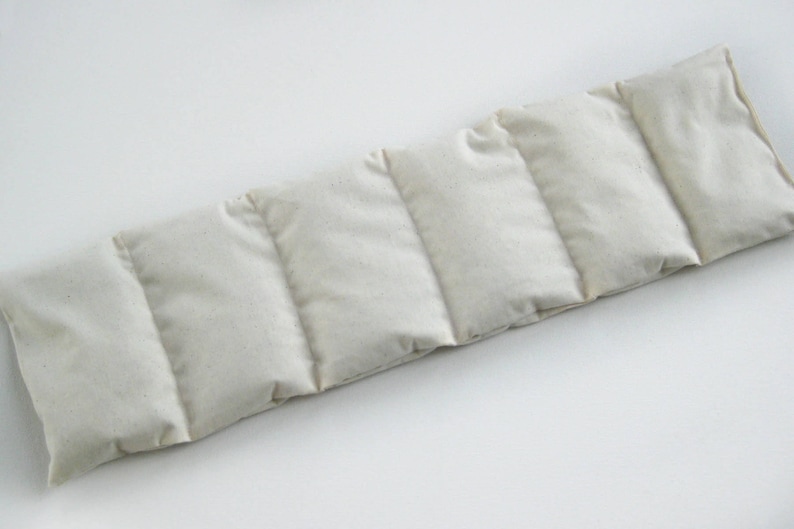 May include: A rectangular, off-white, segmented heat pack. The pack is divided into six sections by vertical stitching. The fabric appears to be a natural, unbleached material. The heat pack is designed to conform to the body.