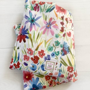 May include: Folded white fabric with a watercolour floral pattern. The design features red, blue, and purple flowers with green stems and leaves. A small tag with the text "Liz King Designs" is attached.
