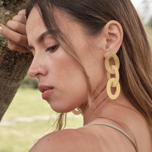 May include: A woman wearing gold chain link earrings. The earrings are made of multiple connected oval shapes.