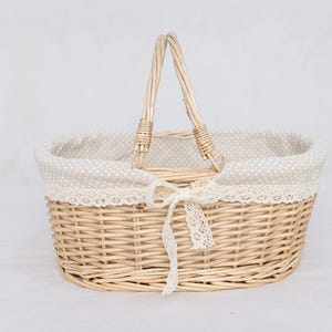 May include: A light brown wicker picnic basket with a handle. The basket has a cream-colored polka-dot lining and is trimmed with lace. A cream-colored ribbon is tied in a bow on the front.