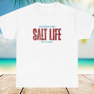 Peut inclure: T-shirt blanc avec un motif rouge et bleu qui dit "California Beach Salt Life Ride the Waves".