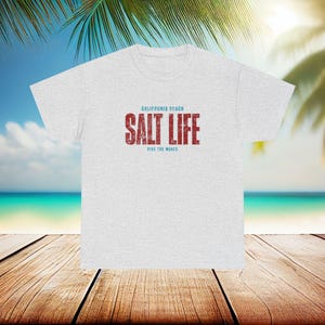 以下が含まれることがあります： グレーのTシャツに「CALIFORNIA BEACH SALT LIFE RIDE THE WAVES」という赤い文字と青い文字で書かれたテキストがあります。