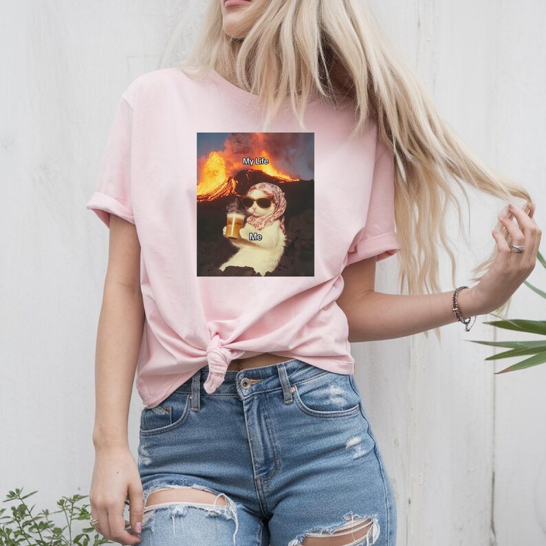May include: Pink t-shirt with a graphic of a cat wearing sunglasses and holding a beer in front of a volcano. The text "My Life" is above the cat and the text "Me" is below the cat.