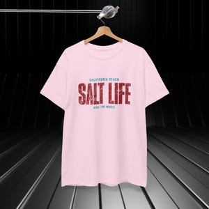Peut inclure: T-shirt rose avec un graphisme rouge qui dit "California Beach Salt Life Ride the Waves".