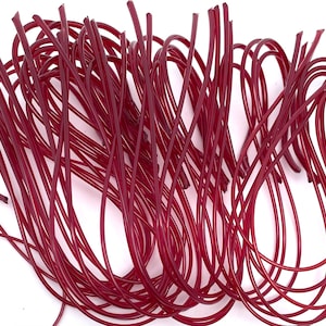 May include: A collection of thin, flexible, burgundy-colored wires, arranged in a tangled pattern against a white background. The wires appear to be made of a smooth, possibly plastic material, and are slightly curved.