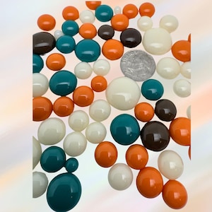 May include: A collection of colorful, round beads in various sizes and shades. The beads are in shades of orange, teal, white, and brown. A silver coin is also present. The beads are scattered across a light background.