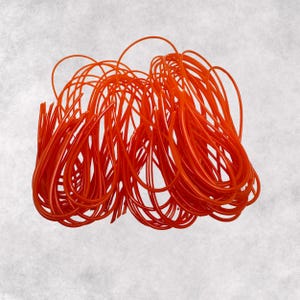 May include: A large bundle of bright orange elastic cord, twisted and tangled together. The cord is thin and flexible, and it appears to be made of a synthetic material.