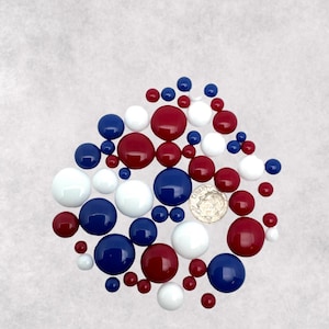 May include: A collection of red, white, and blue glass beads. The beads are various sizes and are arranged in a loose pile.