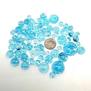 May include: A collection of round, light blue glass beads with a bubbled texture. The beads are scattered on a white surface.
