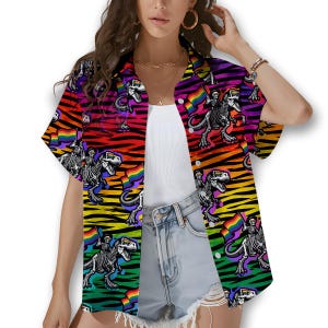 May include: Short-sleeved button-up shirt with a vibrant rainbow zebra stripe pattern. The shirt features a repeating graphic of a skeleton riding a dinosaur and holding a rainbow flag. The shirt is a colorful and unique design.
