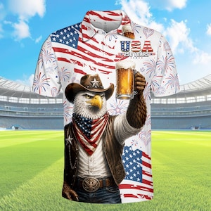 Peut inclure: Polo blanc avec un motif patriotique repr&eacute;sentant un aigle portant un chapeau de cowboy, tenant une bi&egrave;re et un drapeau am&eacute;ricain. Le t-shirt porte le texte "USA 250 YEARS" et un motif de feux d'artifice. Le fond montre un stade et un ciel bleu.
