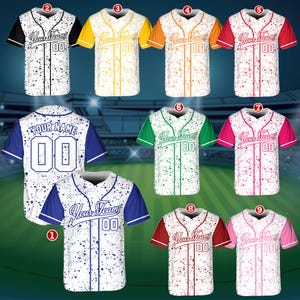 May include: A collection of baseball jerseys in various colors, including white, black, yellow, orange, red, green, and pink. Each jersey features the text "Your Team" and the number "00". The jerseys have a splatter design.