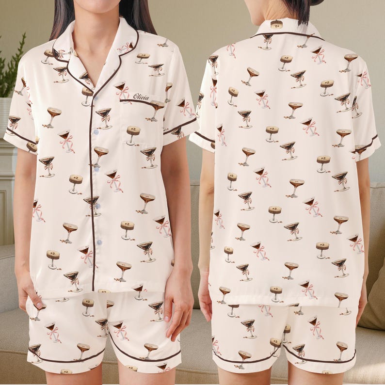 May include: Cream-coloured pyjama set featuring a repeating pattern of martini glasses and pink bows. The short-sleeved top and shorts have dark brown trim. The top has a breast pocket with the name "Olivia" embroidered on it.