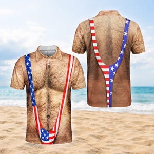 Puede incluir: Un polo de manga corta con un diseño único que presenta un pecho peludo y un patrón de tirantes patrióticos con la bandera estadounidense. La camisa se muestra en una playa de arena con un océano azul y cielo en el fondo.