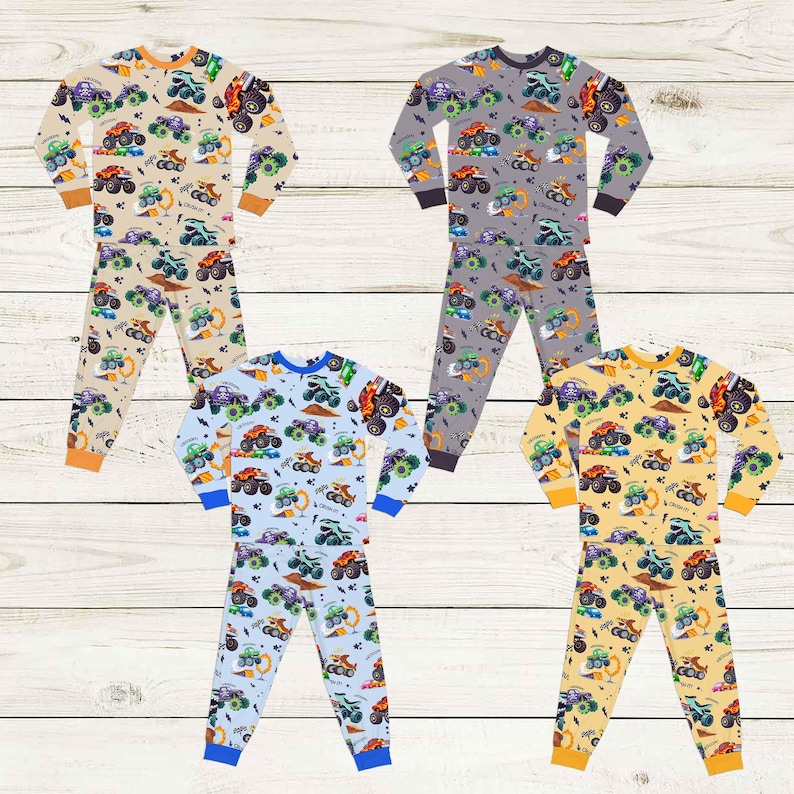 May include: Four sets of children's pajamas with a repeating monster truck pattern. The pajamas are in beige, gray, light blue, and yellow. Each set includes a long-sleeved top and pants. The cuffs and necklines are in contrasting colors.