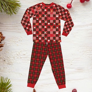May include: A long-sleeve pajama set featuring a red and green checkered top with small holiday-themed graphics including reindeer, snowmen, and Santa Claus, paired with matching red and green plaid pants with solid red cuffs at the wrists and ankles.