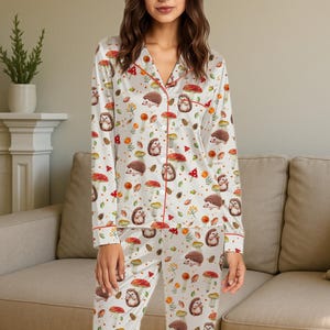 Peut inclure: Ensemble de pyjama blanc avec un motif répété de hérissons, de champignons et de feuillage d'automne. Le haut à manches longues et le pantalon ont une bordure rouge. Le pyjama est en matière douce et soyeuse.