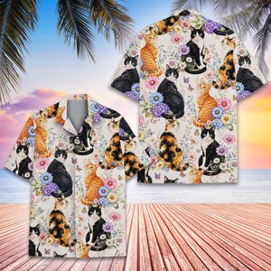 May include: A short-sleeve button-down shirt featuring an all-over print of various cats in black, white, orange, and calico patterns interspersed with colorful flowers, butterflies, and foliage on a light cream-colored background.