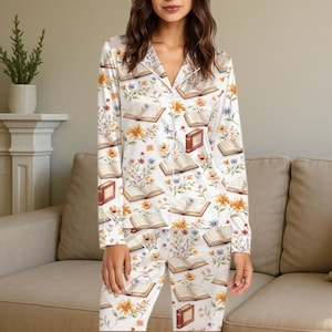 May include: White pyjama set with a floral and book print. The long-sleeved top and trousers feature open books, closed books, and colourful flowers. The pyjamas have a button-down top with a collar.