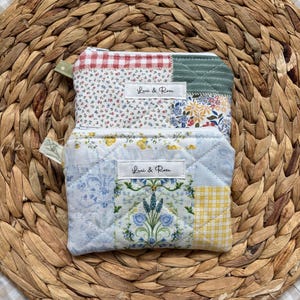 May include: Two small, quilted fabric pouches with patchwork designs. One features floral and gingham patterns, the other has blue floral and yellow gingham patches. Each has a zip and a label that reads "Luci & Rose".