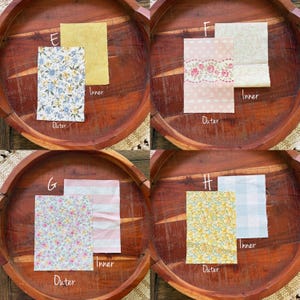 Puede incluir: Cuatro conjuntos de muestras de tela, cada uno con una pieza "Exterior" e "Interior", exhibidos en una bandeja de madera. Las muestras presentan dise&ntilde;os florales, a rayas y estampados en varios colores, incluyendo azul, rosa y amarillo. Las etiquetas "E", "F", "G" y "H" son visibles.