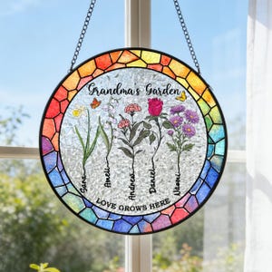 May include: A round stained glass window hanging with a black chain. The window features a colorful mosaic border and a central design of flowers and butterflies. Text reads "Grandma's Garden" and "Love Grows Here."