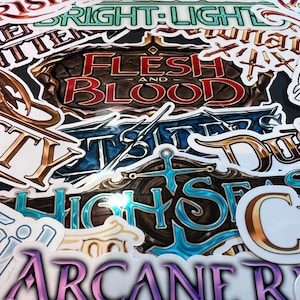Peut inclure: Un ensemble d'autocollants colorés avec du texte et des graphiques. Les autocollants incluent les mots "FLESH AND BLOOD", "HIGH SEAS" et "ARCANE RISING". Les autocollants ont divers motifs et couleurs, notamment le bleu, l'or et le violet.