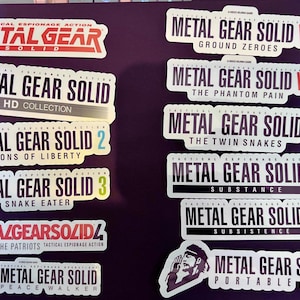 May include: A collection of ten stickers featuring the Metal Gear Solid video game franchise logos. The logos are white with black text and feature different game titles, including Metal Gear Solid, Metal Gear Solid 2, Metal Gear Solid 3, Metal Gear Solid 4, Metal Gear Solid V, Metal Gear Solid HD Collection, Metal Gear Solid: The Twin Snakes, Metal Gear Solid: Substance, Metal Gear Solid: Subsistence, and Metal Gear Solid: Portable Ops.