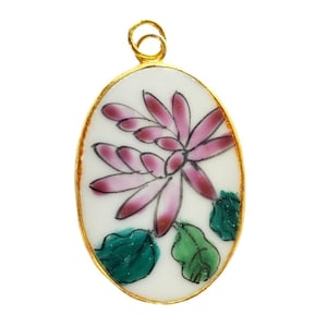 May include: Oval pendant with a gold-colored frame. The pendant features a white background with a pink and red floral design and green leaves. The pendant has a gold-colored loop at the top for hanging.