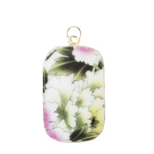 May include: A rectangular ceramic pendant with rounded corners featuring a floral pattern of white, pink, and yellow petals with green leaves. The pendant is framed in a thin gold-toned metal edge and includes a small gold-toned metal bail at the top.