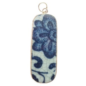 May include: A rectangular pendant with a silver-colored frame. The pendant features a blue and white floral design on a cracked, ceramic-like surface. The top has a small loop for a chain.