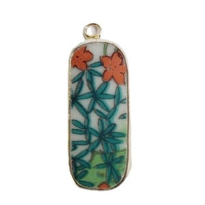 May include: A rectangular pendant with a gold-colored frame. The pendant features a white background with a floral design in orange, green, and teal. The top has a small loop for a chain.