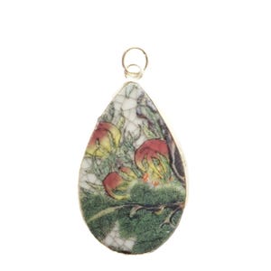 May include: A teardrop-shaped pendant featuring a cracked white ceramic surface with a colorful illustration of red and yellow flowers on green foliage. The pendant is framed in a thin metallic border and includes a small circular metal bail at the top.