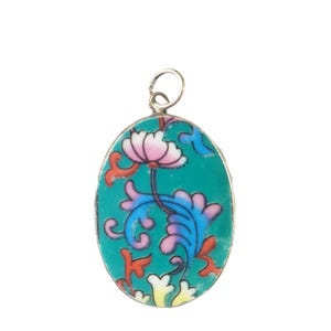 May include: An oval-shaped pendant featuring a vibrant teal background with a central floral motif. The design includes a pink flower at the top, surrounded by swirling blue, pink, and orange leaf-like patterns, all encased in a silver-toned metal frame.