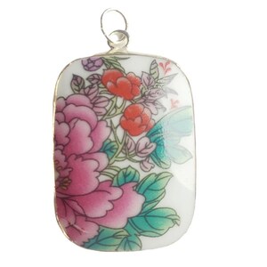 May include: A rectangular pendant with a floral design. The pendant features a large pink peony, red flowers, and green leaves on a white background. A silver loop is at the top for hanging.
