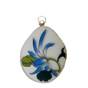 May include: A teardrop-shaped pendant featuring a white background with a painted blue flower design, green leaves, and a dark green leaf at the base. The pendant has a gold-toned metal bail at the top for attachment to a chain or cord.