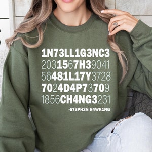 May include: A green sweatshirt with white text that reads "1N73LL1G3NC3 2031567H39041 56481LL17Y3728 7024D4P73709 1856CH4NG3231 -573PH3N H4WK1NG"