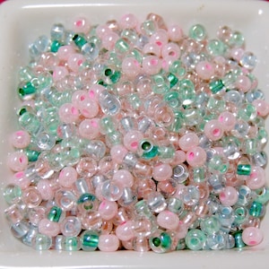 May include: A bowl filled with a variety of small, round beads in shades of pink, green, and clear. The beads have a slightly iridescent finish.