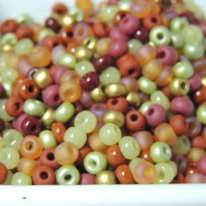 May include: A bowl filled with a variety of small, round beads in shades of green, brown, and red.