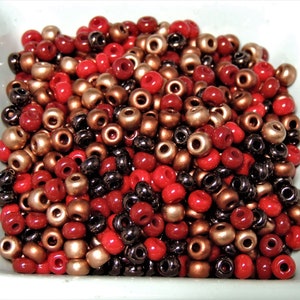 May include: A collection of small, round beads in red, brown, and black colors. The beads are arranged in a random pattern and are suitable for jewelry making or crafting.