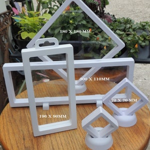 May include: Five white display cases for collectibles. The cases are made of clear plastic and have a white frame. The cases are different sizes, with measurements in millimeters printed on each case. The cases are on a wooden surface.