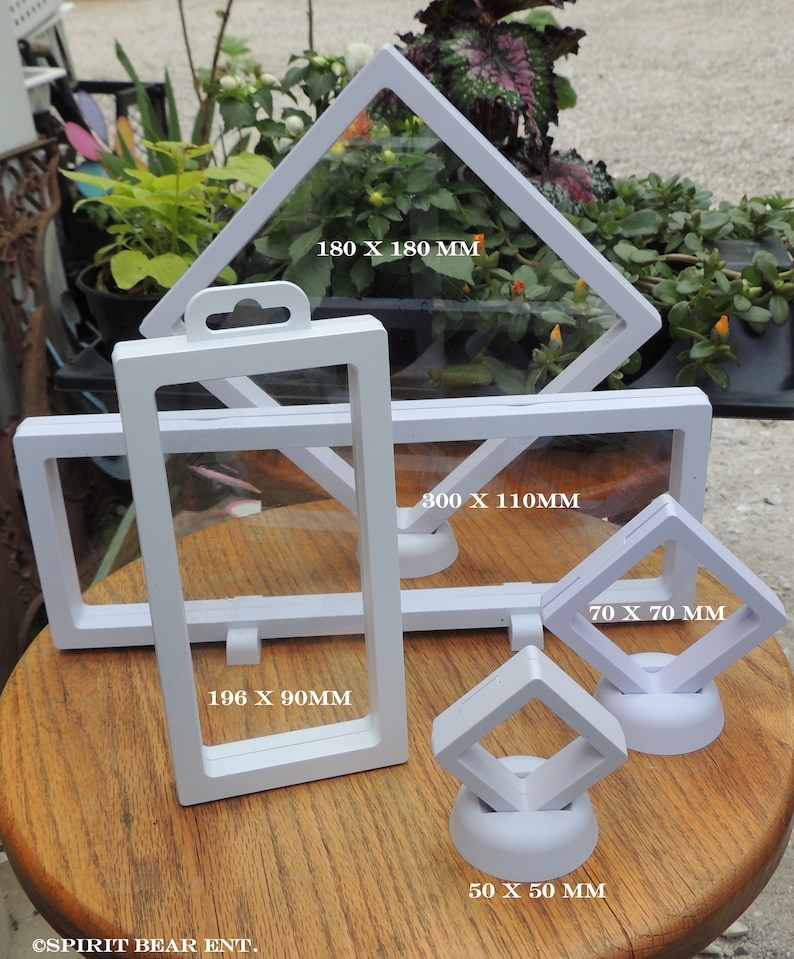 May include: Five white display cases for collectibles. The cases are made of clear plastic and have a white frame. The cases are different sizes, with measurements in millimeters printed on each case. The cases are on a wooden surface.