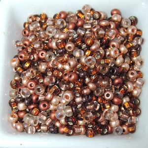 May include: A collection of small, round beads in various shades of brown, copper, and clear glass. The beads are arranged in a random pattern, creating a visually appealing mix of colors and textures.