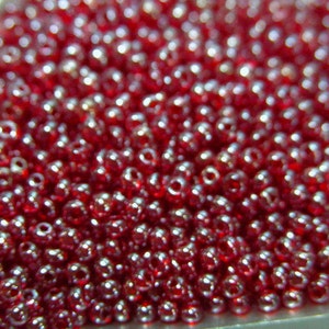 May include: A close-up image of a large quantity of small, round, red beads with a silver iridescent sheen.
