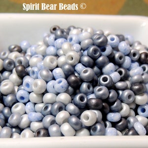 May include: A close-up of a bowl filled with small, round beads in shades of white, blue, and gray. The beads have a slightly iridescent finish.