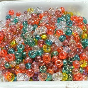 May include: A large assortment of iridescent glass beads in various colors, including clear, pink, green, yellow, and orange. The beads are small and round, and they have a shiny, reflective surface.